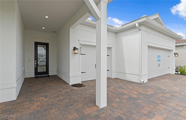 property entrance with a garage, stucco siding, and driveway