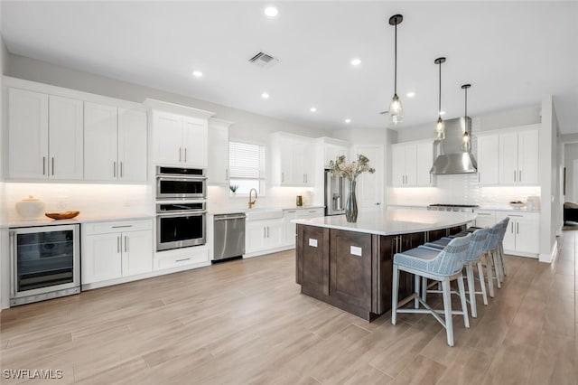15766 Cortina St, Naples, FL 34114 - kitchen featuring appliances with stainless steel finishes, wall chimney range hood, wine cooler, tasteful backsplash, and a breakfast bar area