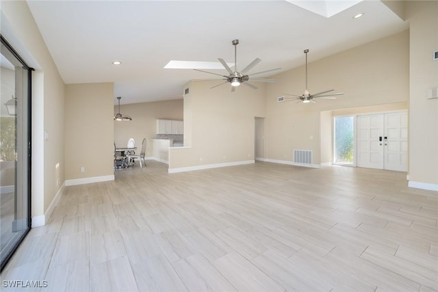 unfurnished living room featuring ceiling fan, vaulted ceiling with skylight, recessed lighting, baseboards, and visible vents