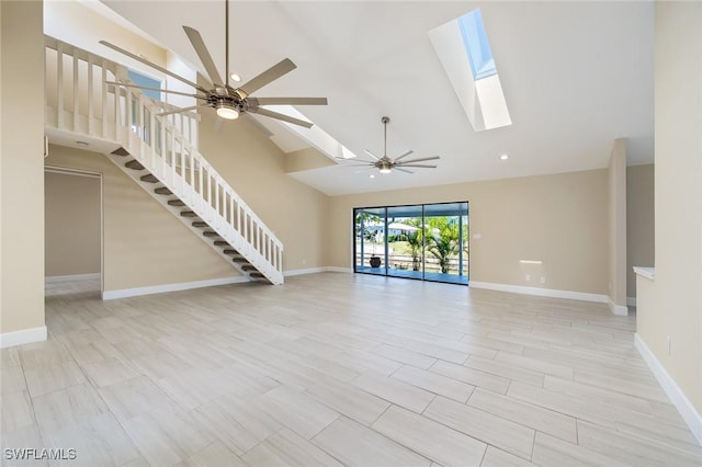 unfurnished living room featuring high vaulted ceiling, a ceiling fan, baseboards, a skylight, and stairway