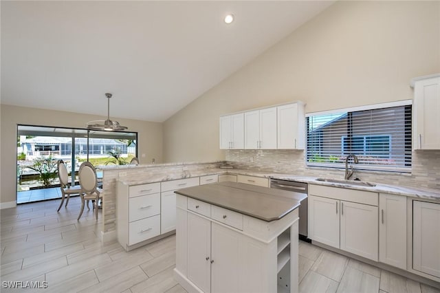 kitchen featuring backsplash, stainless steel dishwasher, a sink, white cabinets, and a peninsula