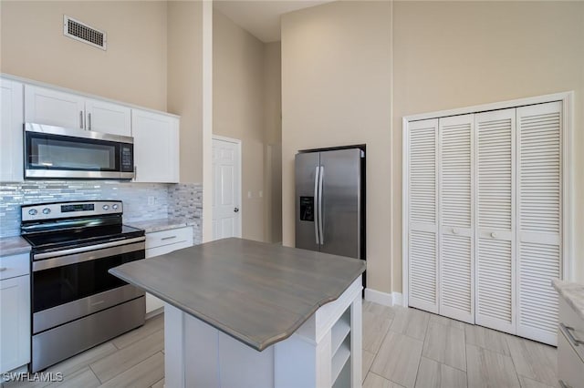 kitchen featuring stainless steel appliances, white cabinetry, backsplash, visible vents, and a kitchen island