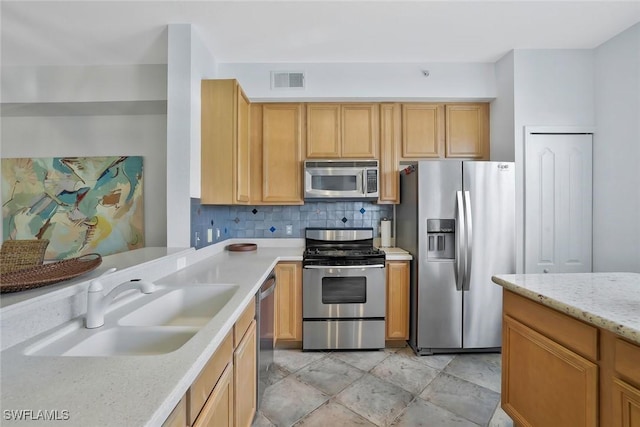 kitchen with light stone countertops, a sink, stainless steel appliances, tasteful backsplash, and visible vents