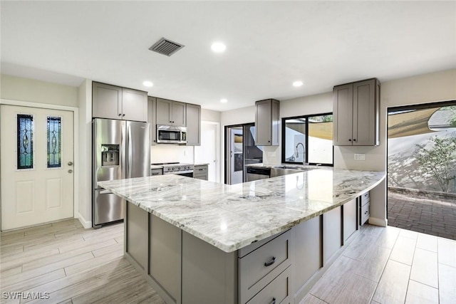 kitchen featuring stainless steel appliances, visible vents, a sink, gray cabinetry, and a peninsula