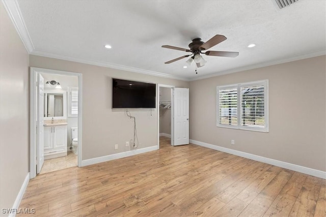 unfurnished bedroom featuring light wood finished floors, ornamental molding, recessed lighting, a walk in closet, and baseboards