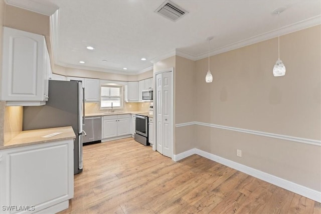 kitchen with appliances with stainless steel finishes, a sink, ornamental molding, light wood-type flooring, and white cabinets