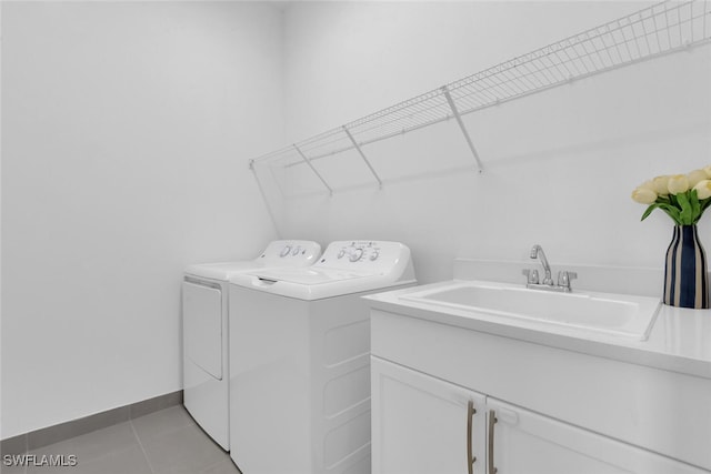 laundry area with washing machine and clothes dryer, cabinet space, a sink, baseboards, and light tile patterned floors