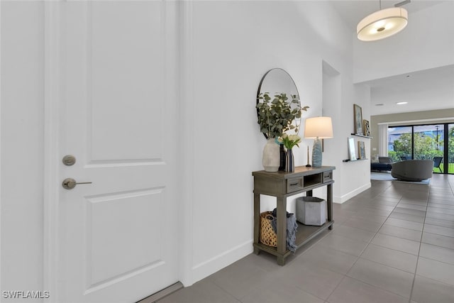 corridor featuring tile patterned flooring, baseboards, and a high ceiling