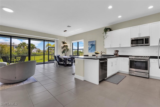 kitchen with dark countertops, appliances with stainless steel finishes, a peninsula, white cabinetry, and tasteful backsplash