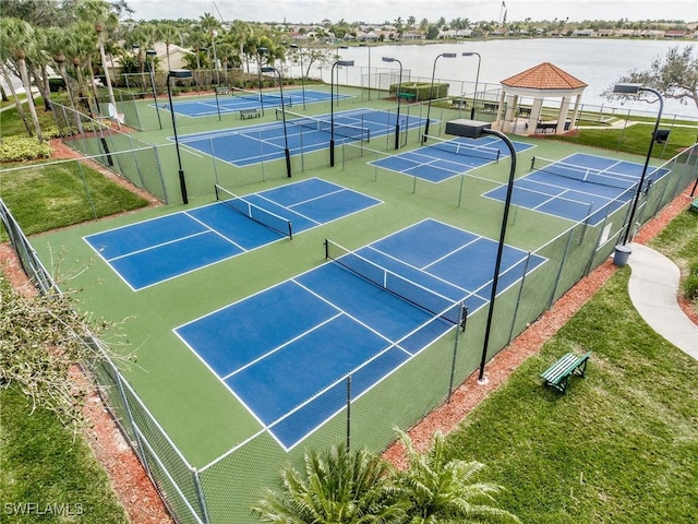 view of tennis court with fence and a water view