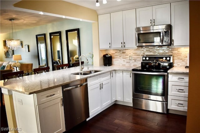 kitchen with a sink, decorative backsplash, a peninsula, appliances with stainless steel finishes, and dark wood-style flooring