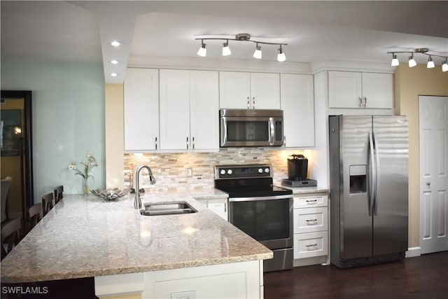 kitchen featuring light stone counters, a sink, white cabinets, a peninsula, and appliances with stainless steel finishes