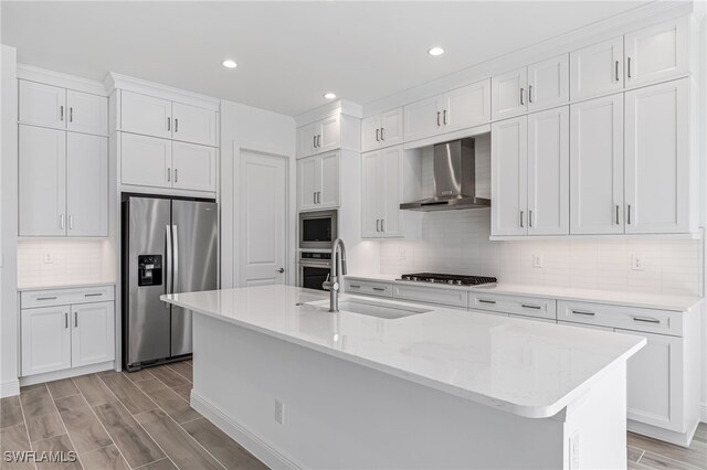 kitchen featuring a sink, light wood-style floors, stainless steel appliances, and wall chimney exhaust hood