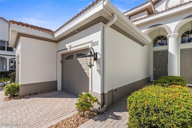 property entrance featuring an attached garage, a tile roof, decorative driveway, and stucco siding