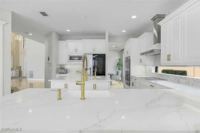 2927 Cinnamon Bay Cir, Naples, FL 34119 - kitchen with stainless steel appliances, wall chimney range hood, tasteful backsplash, recessed lighting, and light stone countertops