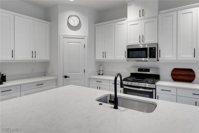 kitchen featuring light stone counters, a sink, white cabinetry, and appliances with stainless steel finishes