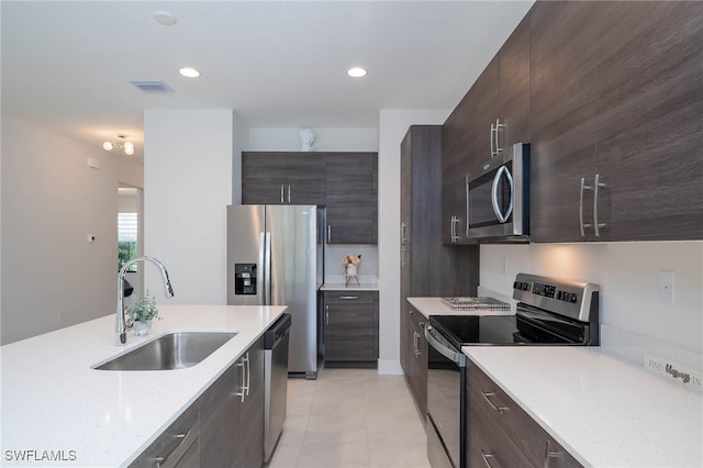kitchen with dark brown cabinetry, light tile patterned floors, appliances with stainless steel finishes, a sink, and modern cabinets