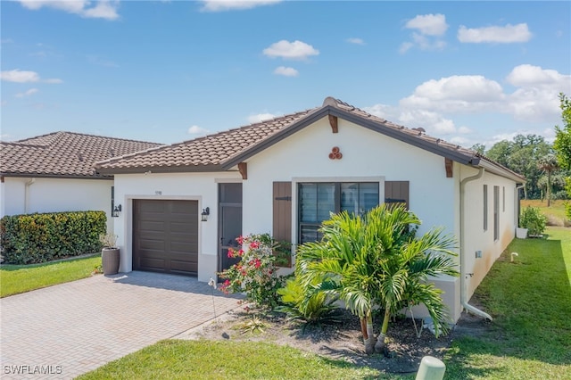 mediterranean / spanish-style home with a tile roof, decorative driveway, an attached garage, stucco siding, and a front lawn
