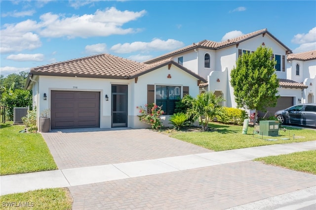 mediterranean / spanish home featuring a front lawn, decorative driveway, central AC, a tiled roof, and an attached garage