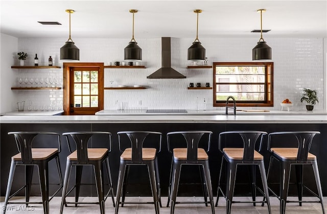 bar with black electric stovetop, a healthy amount of sunlight, tasteful backsplash, and wall chimney range hood