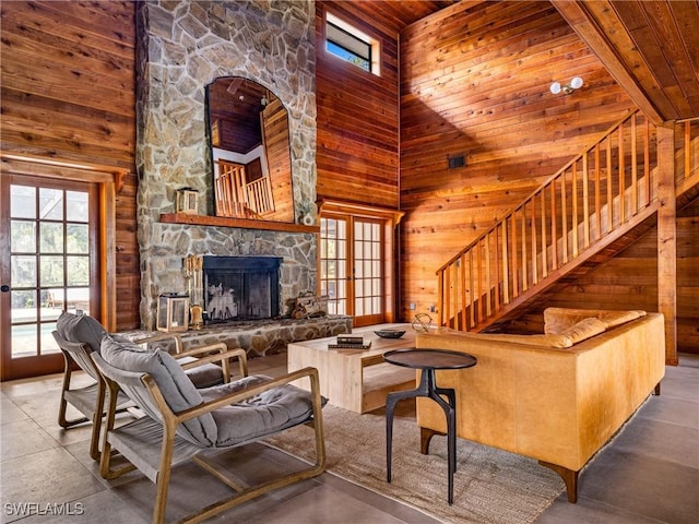 living area with a high ceiling, wooden walls, wood ceiling, a fireplace, and stairs