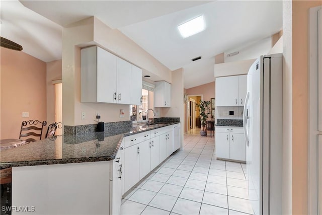 kitchen featuring freestanding refrigerator, a peninsula, white cabinetry, a sink, and vaulted ceiling