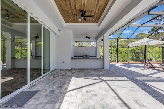view of patio with ceiling fan, glass enclosure, a sink, and exterior kitchen