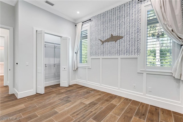 unfurnished bedroom featuring wood finished floors, visible vents, an accent wall, a decorative wall, and wainscoting