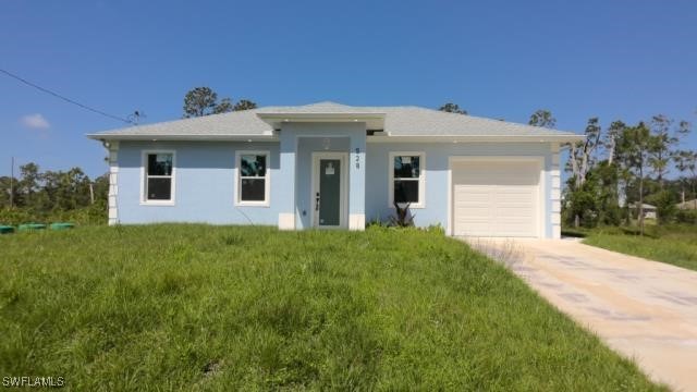 528 Aspen Ave S, Lehigh Acres, FL 33974 - prairie-style home featuring an attached garage, concrete driveway, stucco siding, and a front lawn