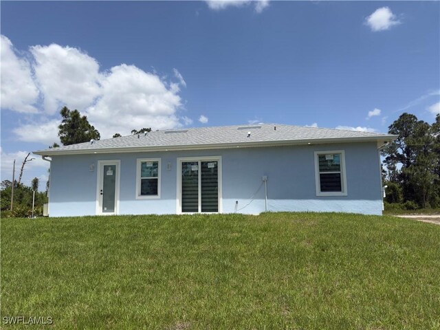 528 Aspen Ave S, Lehigh Acres, FL 33974 - rear view of house featuring stucco siding and a lawn