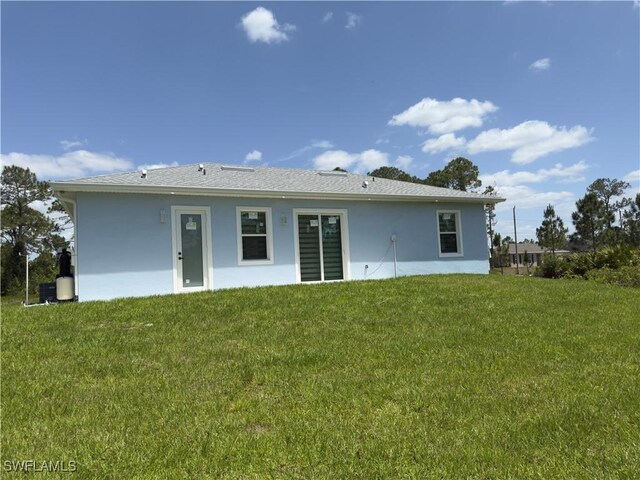 528 Aspen Ave S, Lehigh Acres, FL 33974 - back of house with stucco siding and a lawn