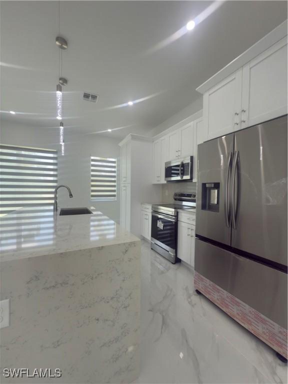 528 Aspen Ave S, Lehigh Acres, FL 33974 - kitchen with appliances with stainless steel finishes, a sink, white cabinets, light stone counters, and light marble finish flooring