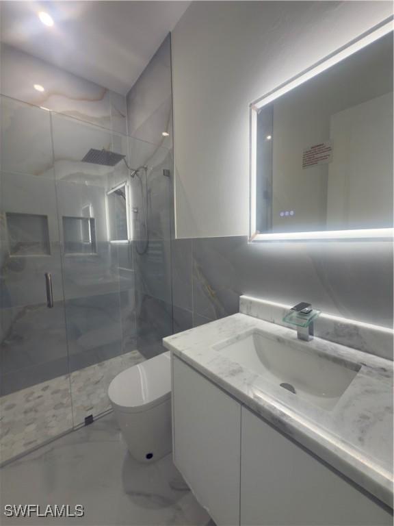 528 Aspen Ave S, Lehigh Acres, FL 33974 - bathroom with marble look tiles, a stall shower, vanity, toilet, and tile walls