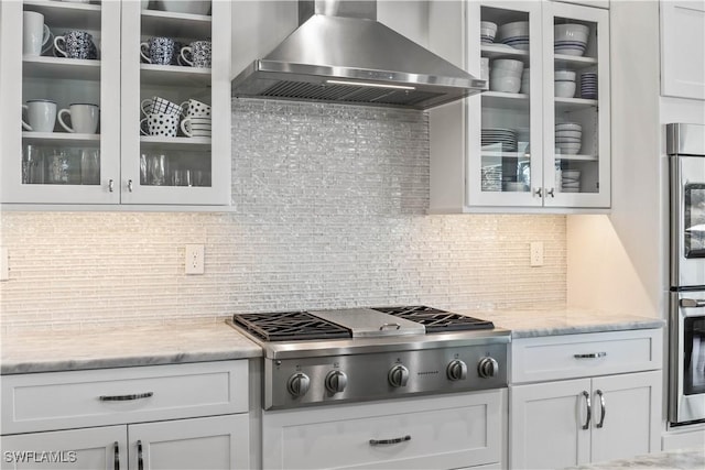 2008 SW 44th Ter, Cape Coral, FL 33914 - kitchen featuring wall chimney range hood, stainless steel gas cooktop, white cabinets, glass insert cabinets, and tasteful backsplash