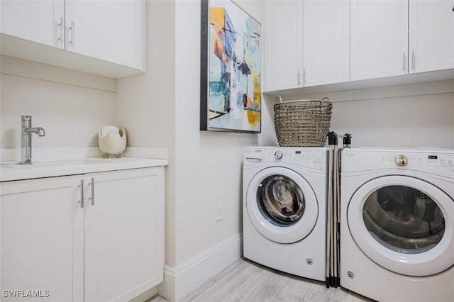 washroom with a sink, cabinet space, washer and clothes dryer, light wood-type flooring, and baseboards