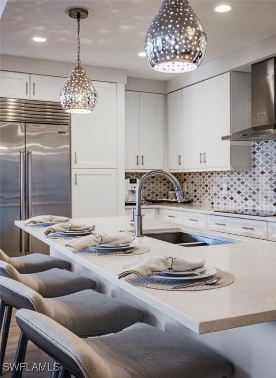 kitchen with decorative light fixtures, stainless steel built in refrigerator, white cabinetry, and wall chimney exhaust hood