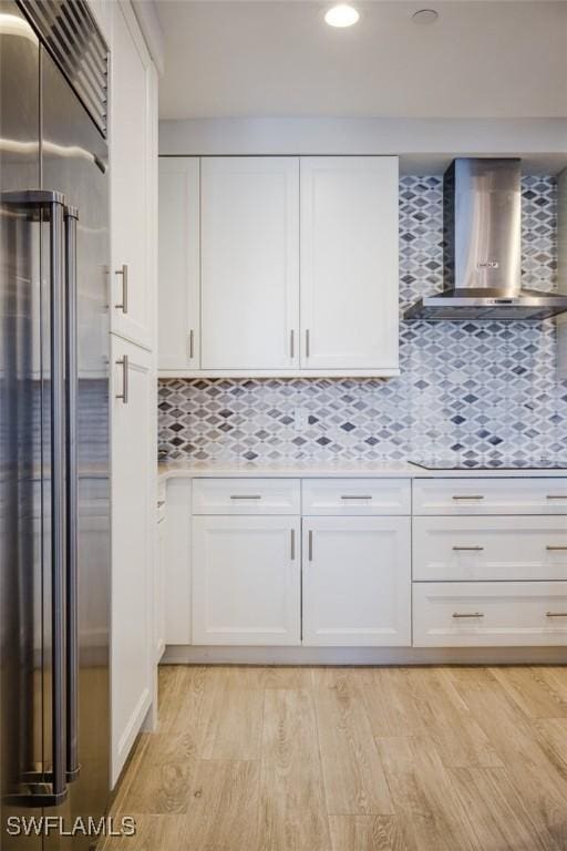 kitchen with wall chimney range hood, high quality fridge, light wood-style flooring, white cabinets, and black electric stovetop