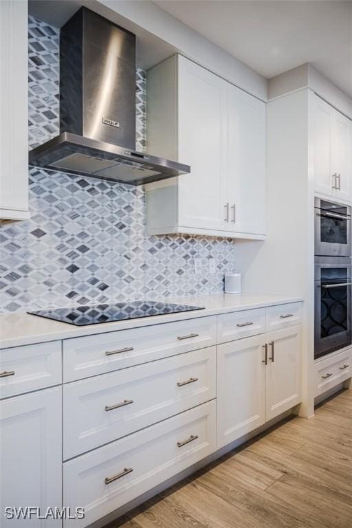 kitchen with white cabinets, light countertops, light wood finished floors, and wall chimney range hood