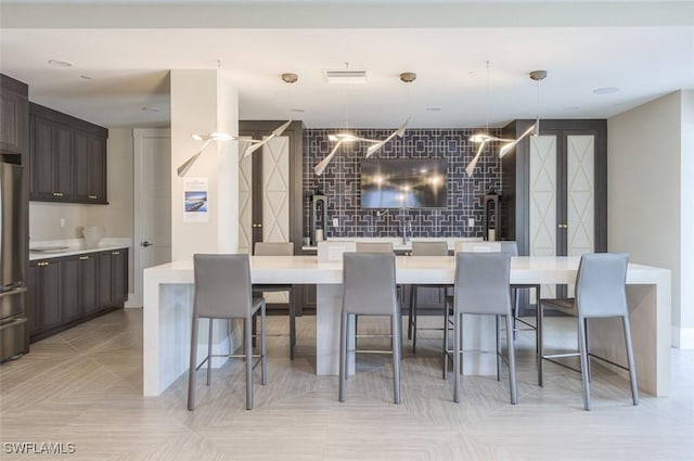 kitchen featuring a kitchen breakfast bar, dark brown cabinetry, visible vents, light countertops, and freestanding refrigerator