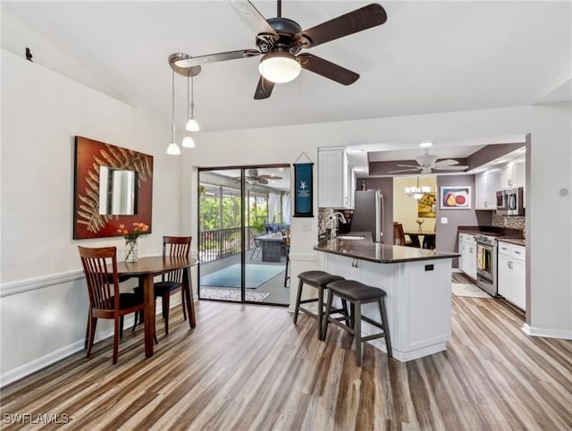 6030 Birnam Wood Ln, Fort Myers, FL 33908 - kitchen with dark countertops, wood finished floors, stainless steel appliances, a peninsula, and white cabinetry