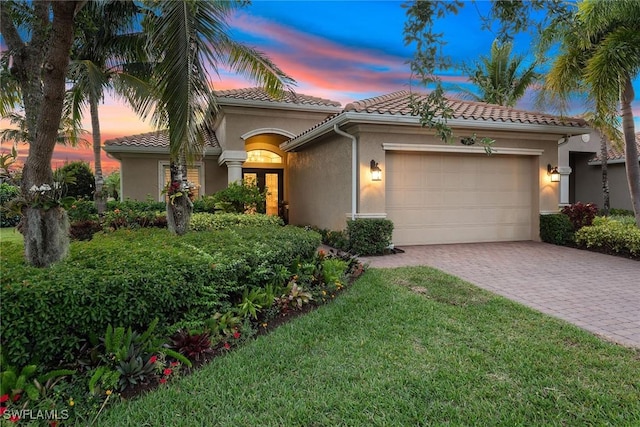 mediterranean / spanish-style house featuring a tile roof, a front yard, decorative driveway, an attached garage, and stucco siding