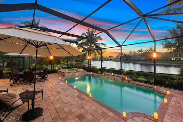 pool at dusk featuring glass enclosure, a water view, a pool with connected hot tub, and a patio area