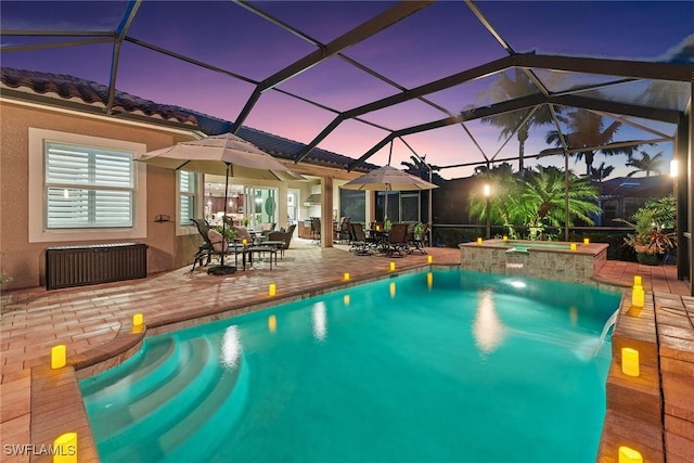 pool at dusk with glass enclosure, a patio, a pool with connected hot tub, and outdoor dining space