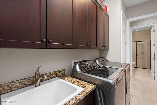 laundry area with cabinet space, light tile patterned floors, washer and clothes dryer, and a sink