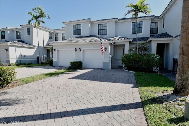 view of property featuring stucco siding, an attached garage, a tile roof, and decorative driveway