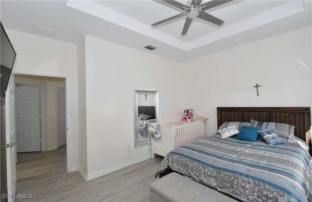 bedroom with baseboards, visible vents, light wood-style floors, a ceiling fan, and a raised ceiling