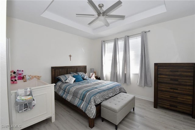 bedroom featuring light wood finished floors, baseboards, a ceiling fan, and a tray ceiling