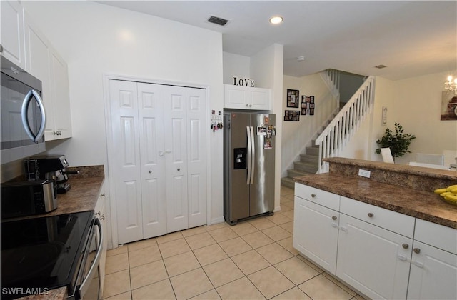 kitchen featuring stainless steel appliances, light tile patterned flooring, dark countertops, visible vents, and white cabinetry