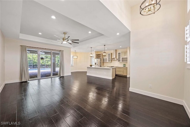 unfurnished living room with baseboards, dark wood-type flooring, and a raised ceiling