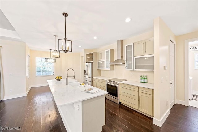 kitchen with wall chimney exhaust hood, a sink, a center island with sink, dark wood-type flooring, and appliances with stainless steel finishes